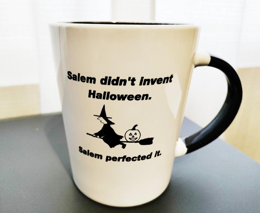 "Salem didn't invent Halloween." "Salem perfected it." White, ceramic, 13oz coffee mug with black handle and interior.
