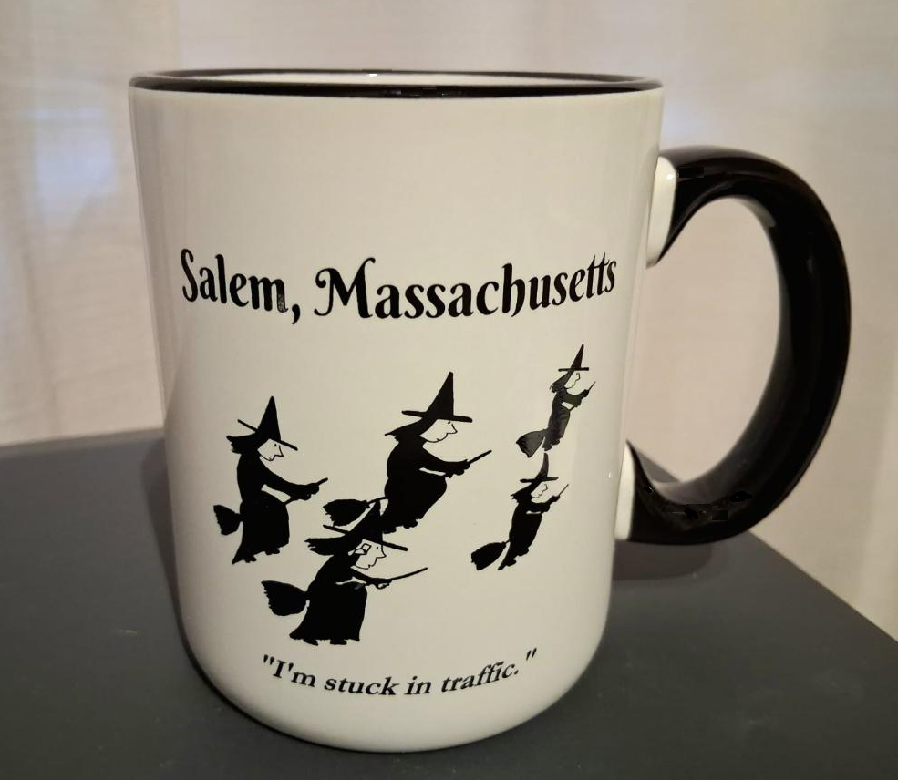 Salem, Massachusetts "I'm stuck in traffic." White, ceramic, 12oz coffee mug with black handle and rim with white interior.