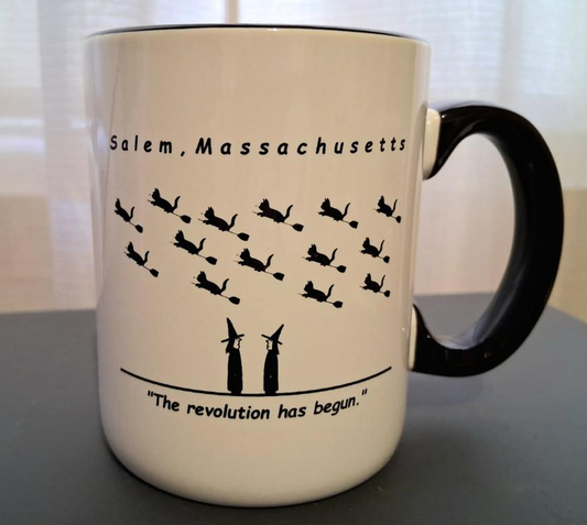 Salem, Massachusetts "The revolution has begun" White, ceramic, 12oz coffee mug with black handle and rim with white interior.