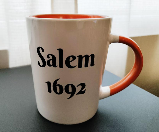 "Salem 1692" "Never again" White, ceramic, 13oz, two-sided coffee mug with orange handle and interior.